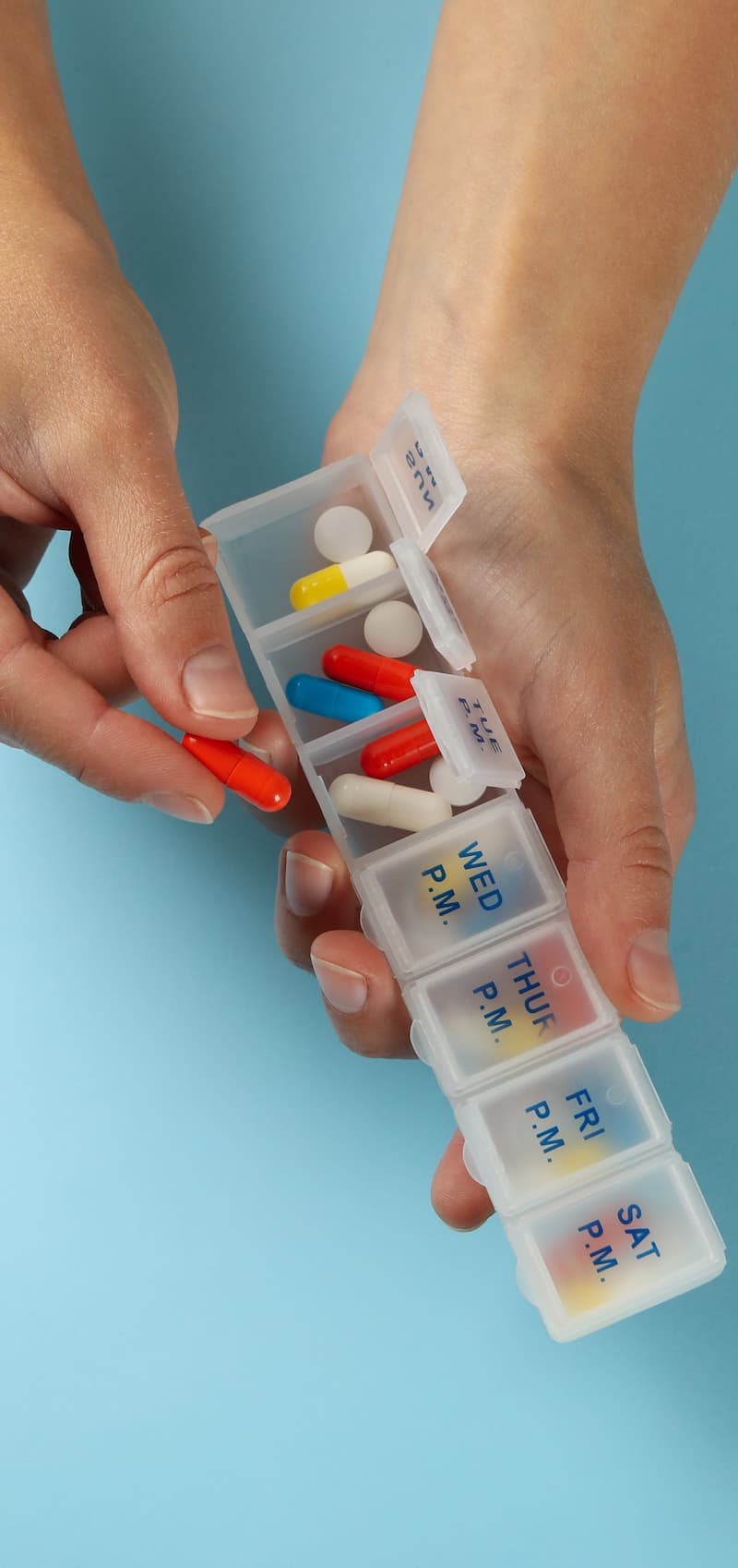 female-hands-hold-containers-with-pills-on-blue-ba